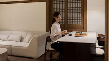 A person seated at a table with a traditional tea set, a sofa, and a wooden partition in the background.