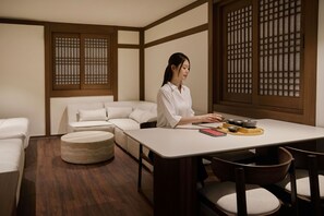 Una habitación con un sofá blanco, un reposapiés redondo, una mesa de madera con una bandeja de cuencos, y puertas correderas de madera tradicionales.