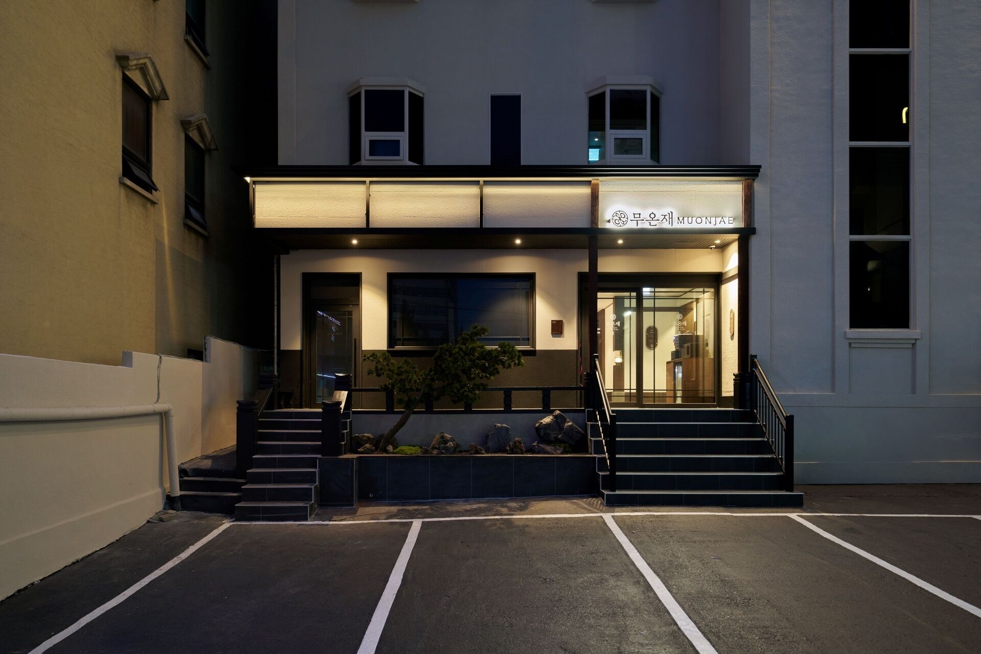 Um edifício com entrada iluminada, escadaria e um pequeno jardim.