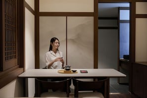A person seated at a table with a traditional tea set, in a room with sliding doors and a view of a mountain. - Muonjae by Anook Daejeon Terminal Complex (Daejeon)