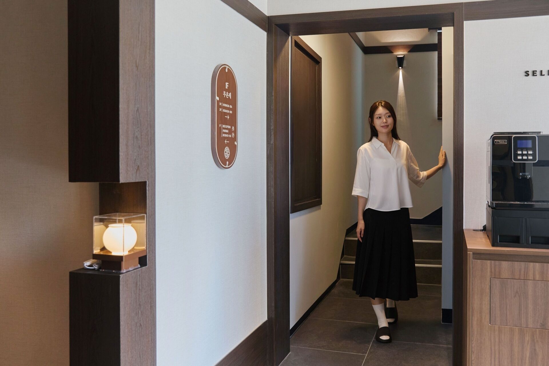 A hotel corridor with a reception desk, a sign with room numbers, and a water dispenser.