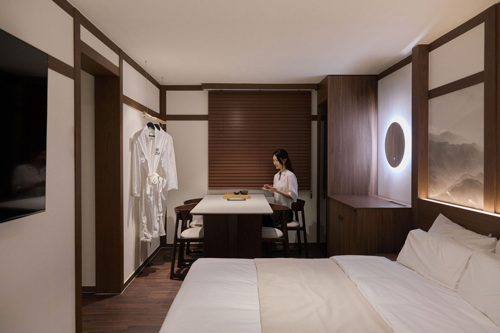 Una habitación de hotel con cama, mesa de comedor, televisor y una obra de arte en la pared.