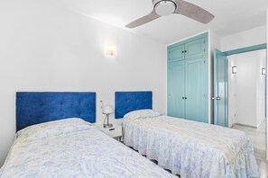 A hotel room with two beds, a ceiling fan, a nightstand with a lamp, and a light-colored wall. - Sea Views of Africa & Pool | Calahonda (Mijas)