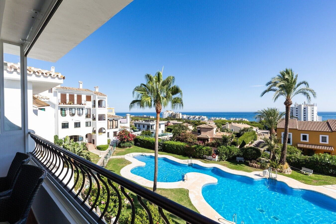 A pool area with a view of the sea, surrounded by buildings and palm trees.