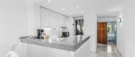 A modern kitchen with a granite countertop, white cabinetry, and a coffee maker.