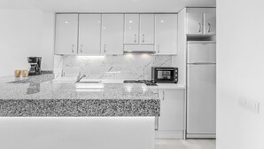 Cozinha moderna com armários brancos, bancada de granito, cafeteira, micro-ondas e geladeira.