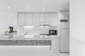 Eine moderne Küche mit weißen Schränken, einer Granitabdeckung, einer Kaffeemaschine, einer Mikrowelle und einem Kühlschrank.