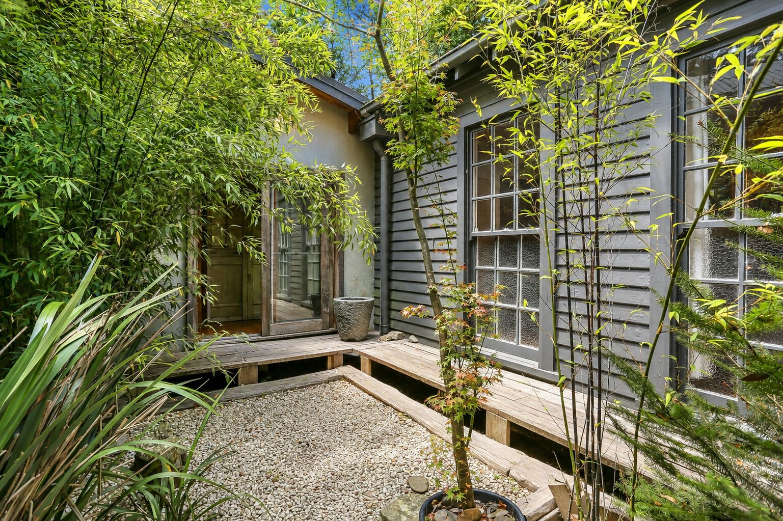 A garden with a wooden deck, a stone pathway, and a variety of plants.