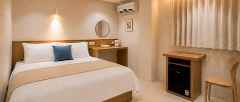 A hotel room with a bed, bedside table, a small cabinet, a chair, an air conditioning unit, and a window with curtains.