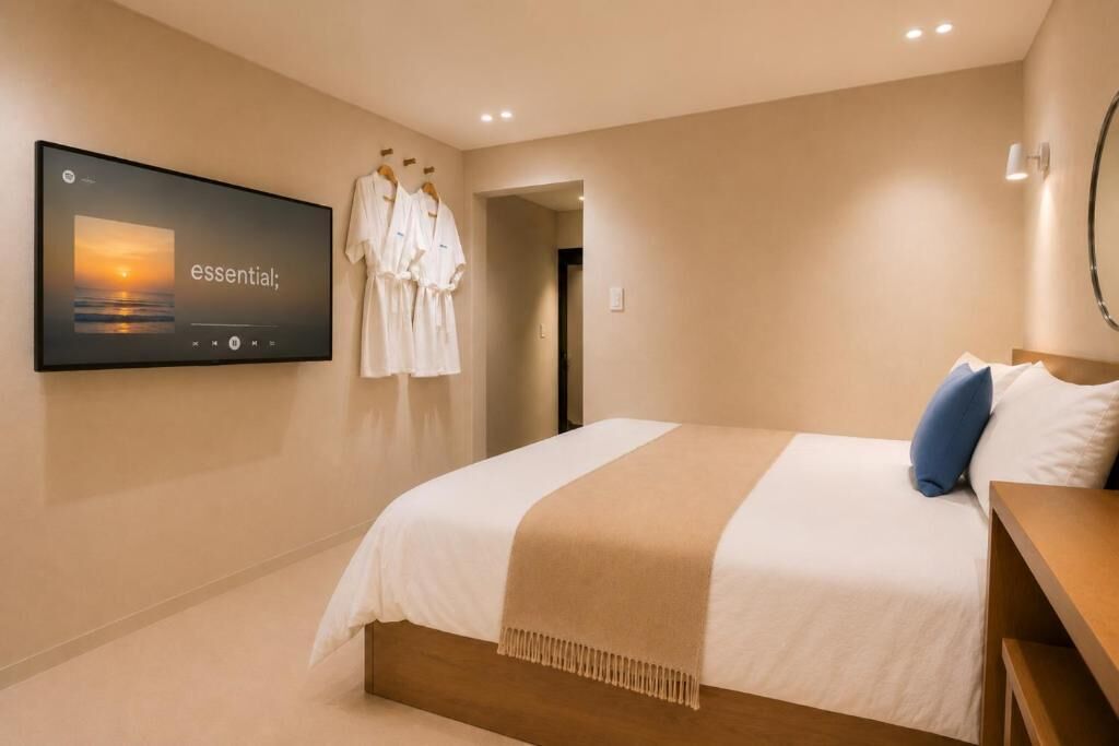 A hotel room with a bed, a TV mounted on the wall, and a robe rack with robes.