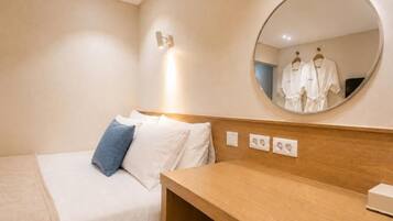 Habitación de hotel con cama, mesita de noche, espejo y lámpara de pared.