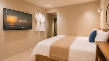 A hotel room with a bed, a TV on the wall, and a robe rack.