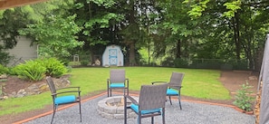 A patio area with a fire pit, outdoor furniture, and a garden with a shed in the background. - Come getaway to a cozy Little 2-bedroom cabin in Arlington/Granite Falls area. (Arlington)