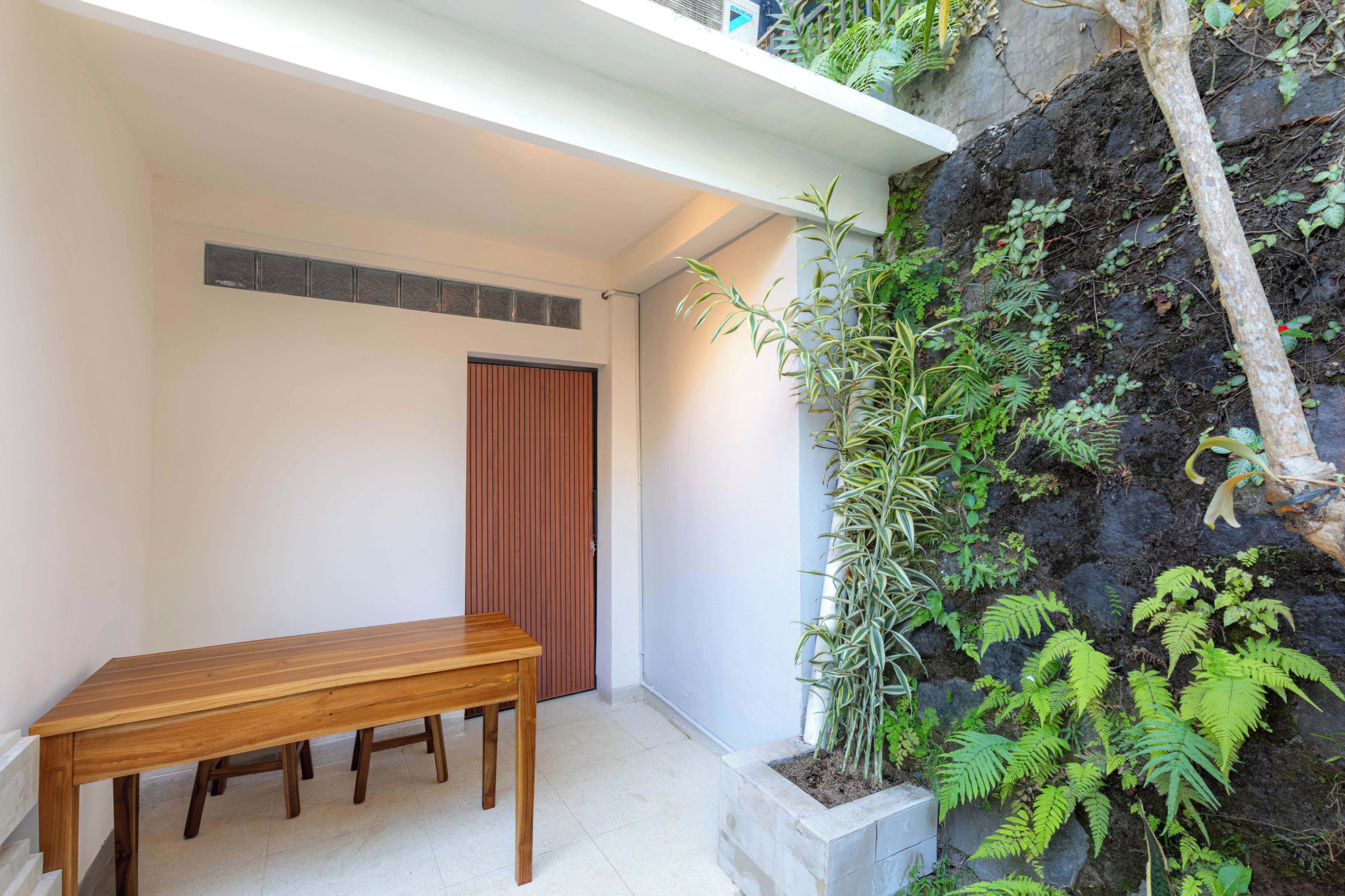 Una mesa y banco de madera en un rincón, con pared blanca y puerta.