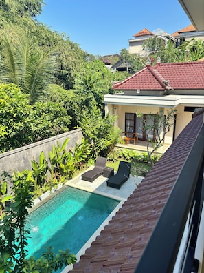 A residential property with a swimming pool, lounge chairs, and a red-tiled roof.
