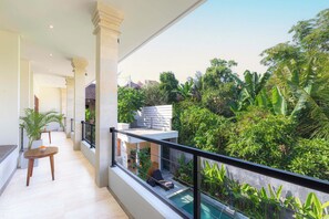 A balcony with a pool, surrounded by lush greenery and a view of a residential area.