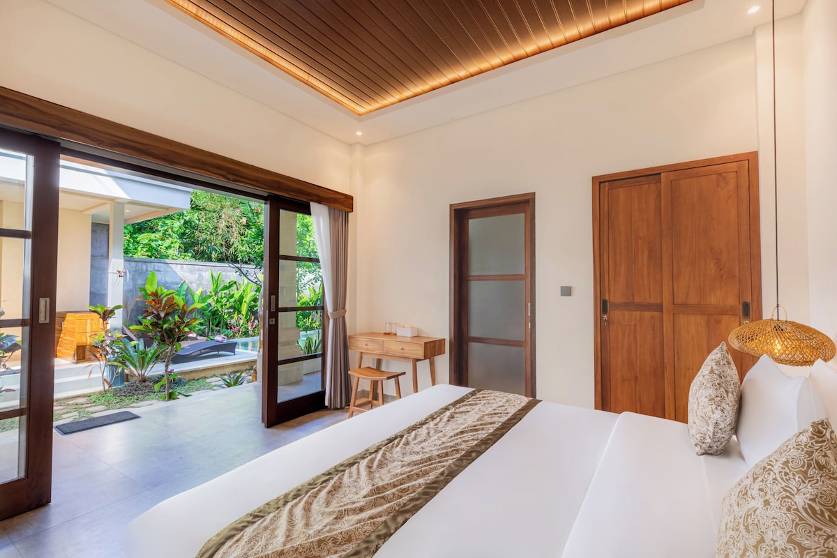 Quarto com uma cama grande, uma escrivaninha e vista para um jardim através de portas de vidro.
