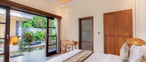 A bedroom with a large bed, a desk, and a view of a garden through glass doors.