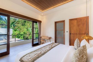 A bedroom with a large bed, a wooden desk, and a view of greenery through the window.