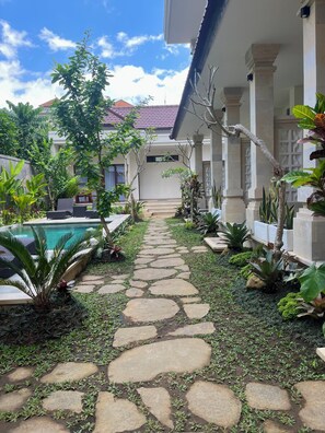 A stone pathway leading to a pool area with lush greenery and a building with columns.