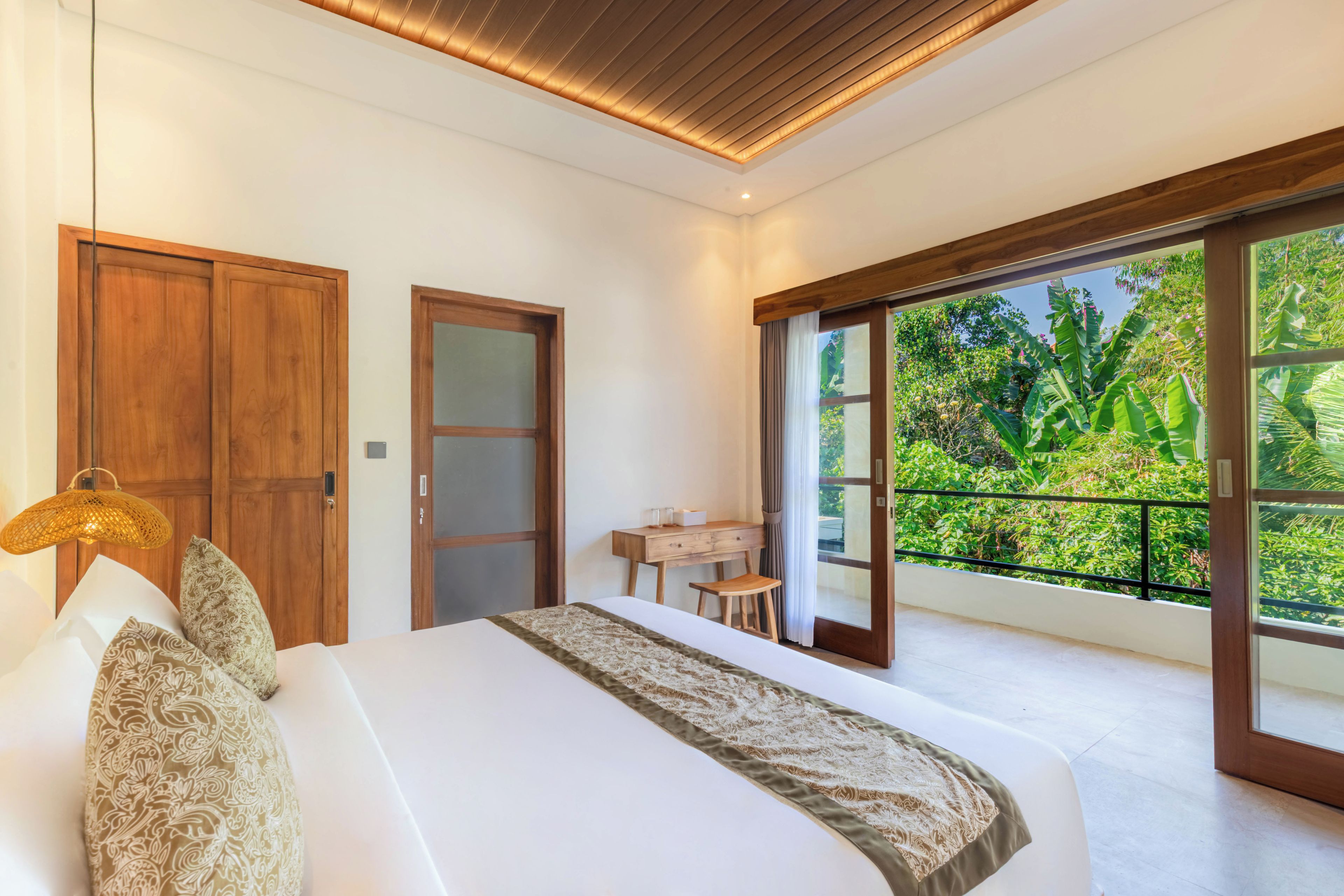 Un dormitorio con una cama grande, un armario de madera, un escritorio con silla y un balcón con vistas a zonas verdes.