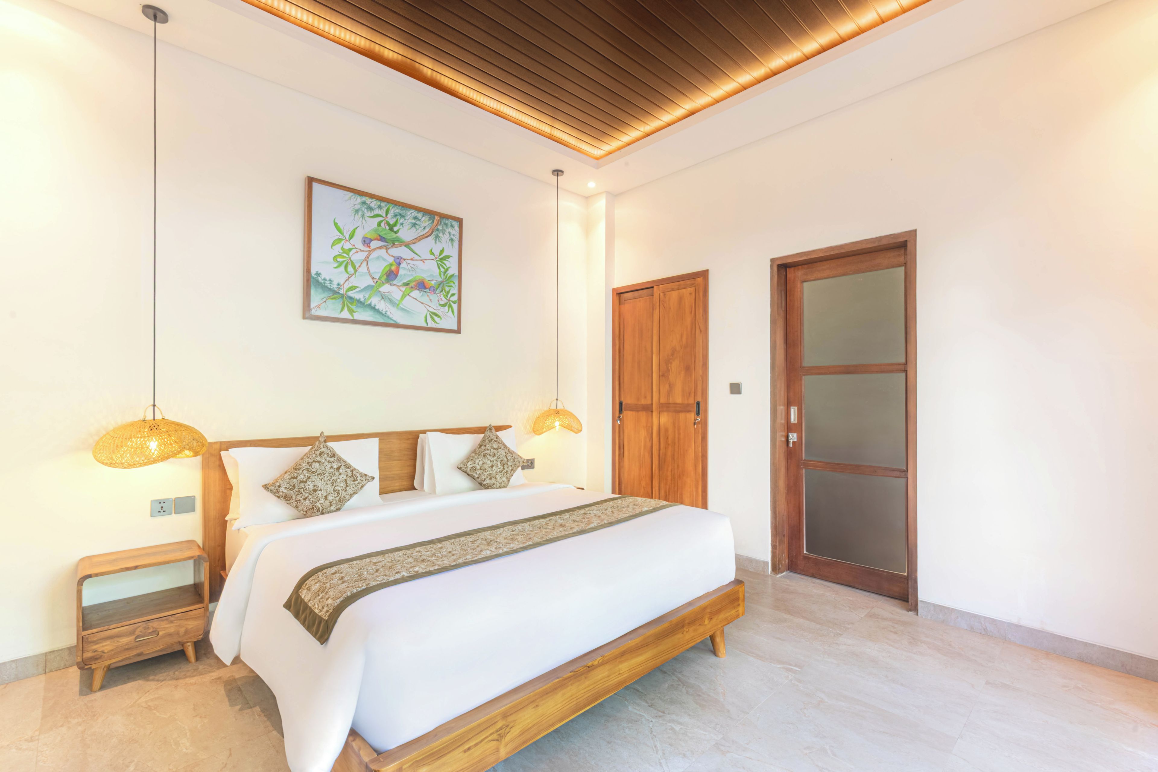 Un dormitorio con una cama grande, dos mesitas de noche, un armario de madera y una puerta con paneles de vidrio esmerilado.