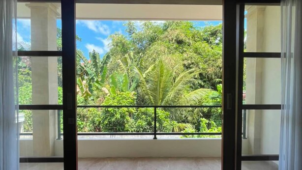 Una habitación con un amplio ventanal corredera que da a un balcón con vistas a exuberante vegetación y un cielo despejado.