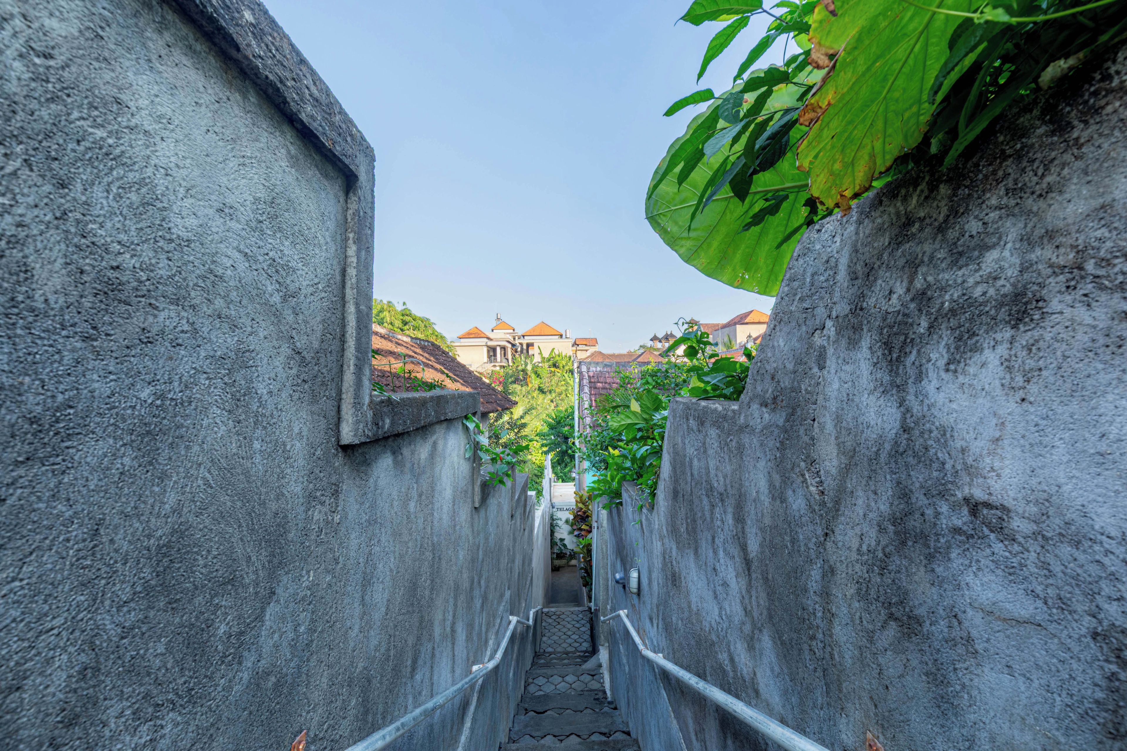 A narrow concrete pathway flanked by walls, leading to a building with a tiled roof.