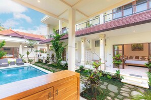 Um edifício de dois andares com piscina, área de estar ao ar livre e diversas plantas.