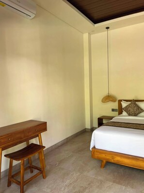 A bedroom with a wooden bed, a bedside table, a desk, and a hanging light fixture.