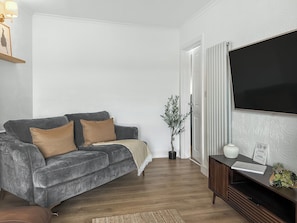 A living room with a grey sofa, a flat-screen TV, a wooden coffee table, and a potted plant. - 3 bedroom accommodation in Tweedmouth (Tweedmouth)