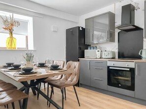 A modern kitchen with grey cabinets, a built-in oven, and a dining area with a table set for four. - 3 bedroom accommodation in Tweedmouth (Tweedmouth)