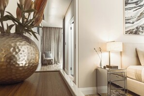 Ein modernes Hotelzimmer mit Holzboden, einem kleinen Nachttisch mit Lampe, einer Couch und einer großen Vase mit Pflanzen.