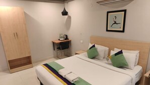 Habitación de hotel con una cama grande, un escritorio con una silla, un armario y un cuadro en la pared.