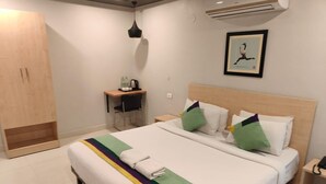 Habitación de hotel con una cama grande, un escritorio con silla, un armario y un cuadro en la pared.