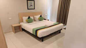 Una cama bien hecha con cabecera de madera, una mesita de noche y un teléfono instalado en la pared.