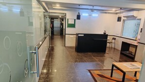 Un área de recepción con mostrador, pared de vidrio, piso de baldosas y ventilador de techo.