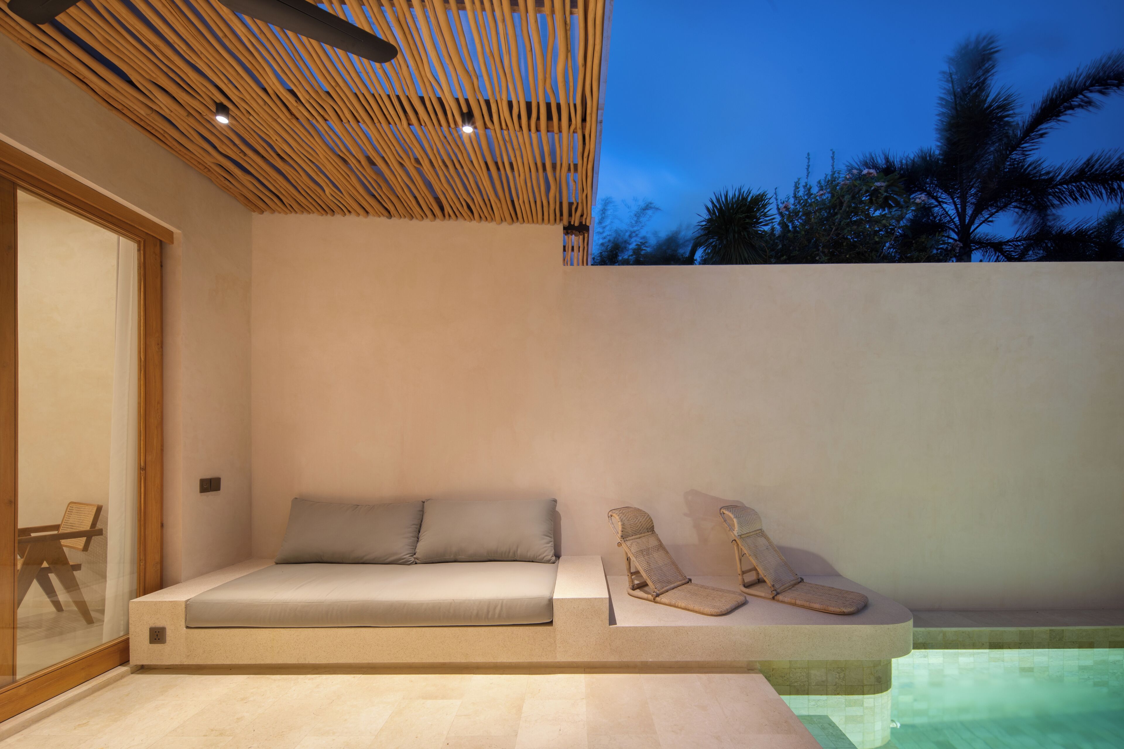 A modern outdoor seating area with a sofa and two lounge chairs, a pool, and a wooden ceiling structure.