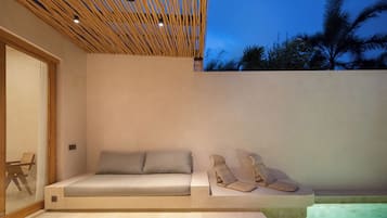A modern outdoor seating area with a sofa and two lounge chairs, a pool, and a wooden ceiling structure.