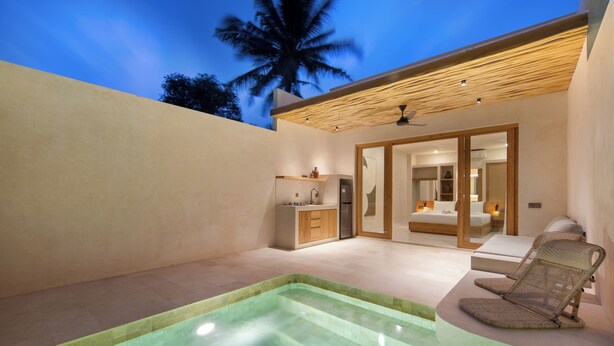 Uma área moderna de piscina ao ar livre com hidromassagem, espaço para sentar e um quarto visível por uma porta aberta.