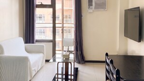 A room with a bed, a desk, a chair, a television, a window with curtains, and an air conditioning unit.