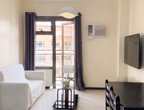 A room with a bed, a desk, a chair, a television, a window with curtains, and an air conditioning unit.