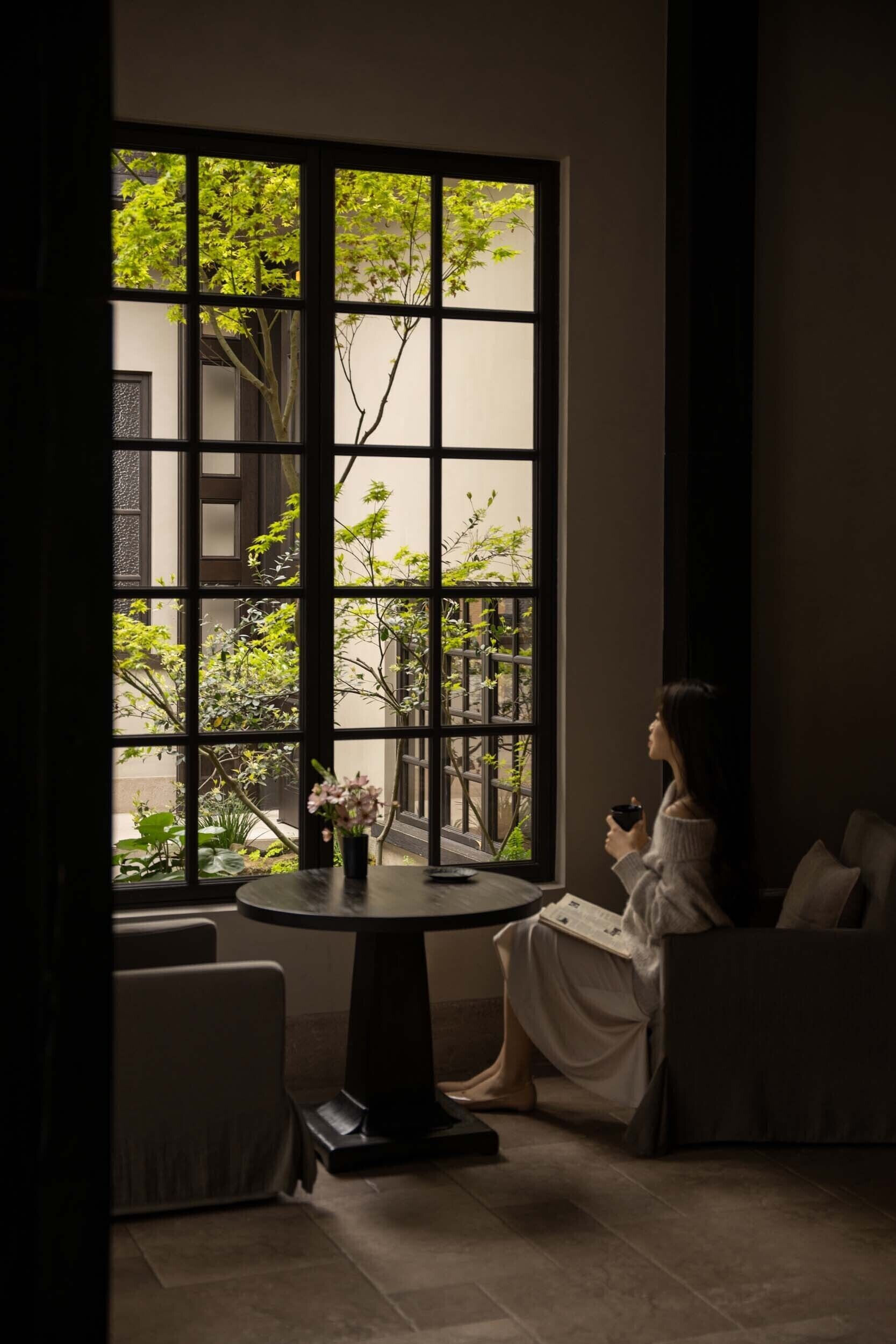 A room with a large window, a round table, and a person seated.
