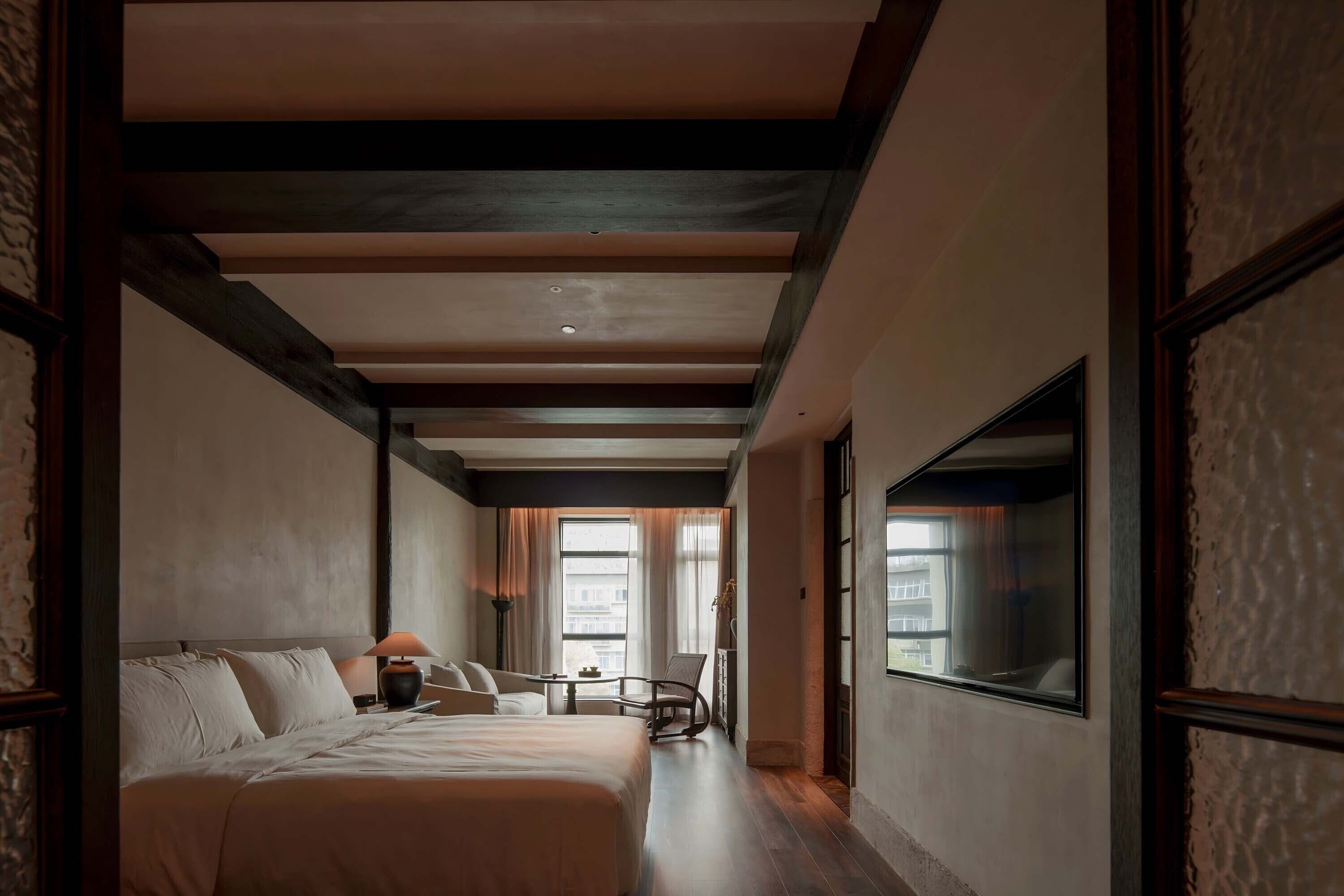 A hotel room with a large bed, a desk, a chair, and a window.