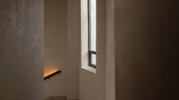A narrow stairway leading to a landing with a window, a wall-mounted shelf, and a textured floor.