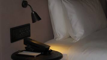A hotel room with a bed, a bedside table, a lamp, and a power outlet.