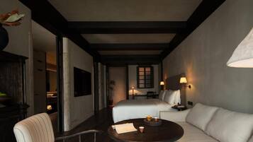 A hotel room with a bed, a sofa, a round table with a lamp, and a chair.
