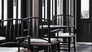A dining area with chairs and tables arranged in rows, a tall floor lamp, and a door with vertical blinds.