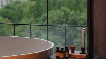 A room with a large bathtub, a small table with candles, and a view of a cityscape through a window.