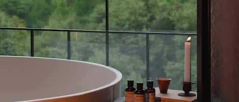 A room with a large bathtub, a small table with candles, and a view of a cityscape through a window.